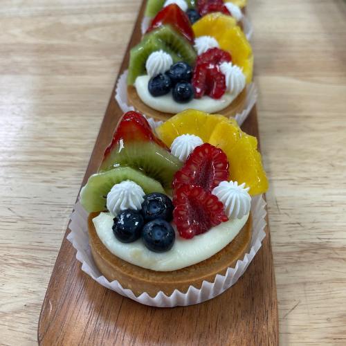 Colorful fruit tarts topped with kiwi, strawberries, blueberries, and whipped cream on a wooden tray.