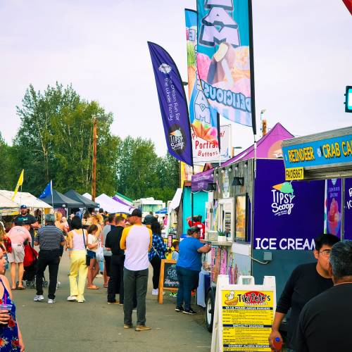 A lively outdoor market scene with food stalls, colorful banners, and people enjoying the festivities.