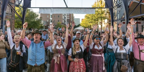 A lively crowd in traditional attire raises their hands in celebration at an outdoor event.