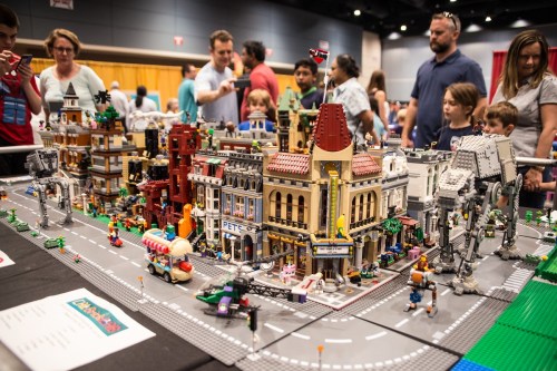 A vibrant LEGO city display with detailed buildings and figures, surrounded by an engaged crowd at an event.