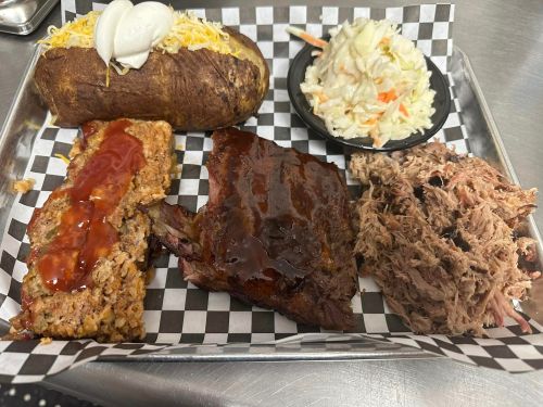 A metal tray with a baked potato topped with cheese, pulled pork, ribs, meatloaf with sauce, and a side of coleslaw.