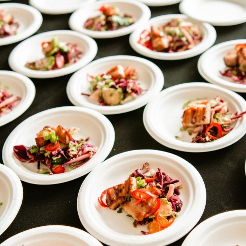 Plates of colorful salad with grilled meat, garnished with herbs and vegetables, arranged on a black table.