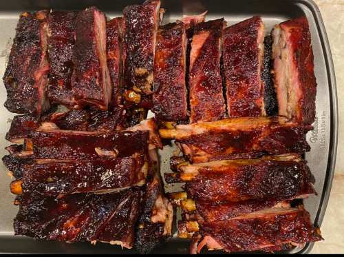 A tray of perfectly cooked, glazed barbecue ribs, sliced and arranged neatly.