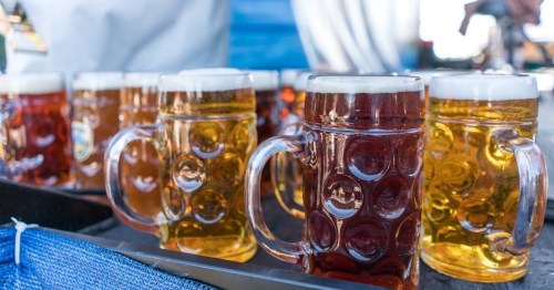 A variety of beer mugs filled with golden and amber brews, arranged on a tray at an outdoor event.
