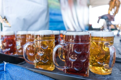 A tray of frothy beer mugs in various shades, including amber and golden, set against a blurred background.