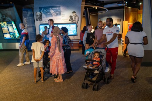 A diverse group of people, including children in strollers, exploring an exhibit in a museum.