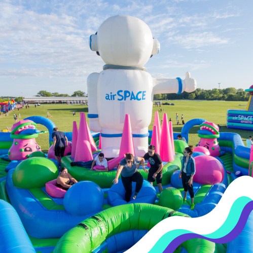 A colorful inflatable playground with a large robot figure, featuring slides and playful structures, set in a grassy field.