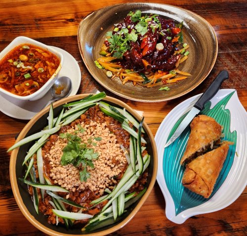 A table with three dishes: spicy soup, stir-fried vegetables, and a bowl of noodles topped with cucumber and peanuts.
