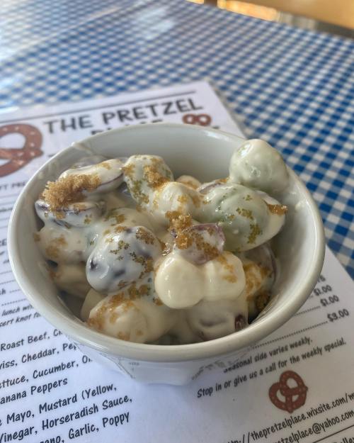 A bowl of colorful popcorn drizzled with white and green sauces, sprinkled with seasoning, on a checkered tablecloth.