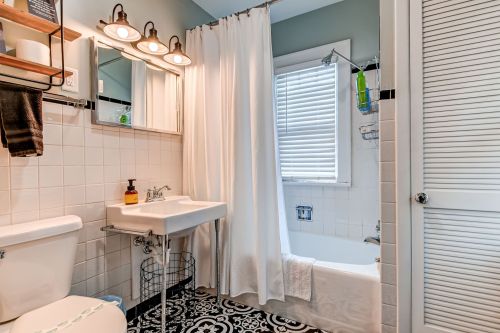 A modern bathroom featuring a white sink, bathtub with shower, and decorative black and white tile flooring.