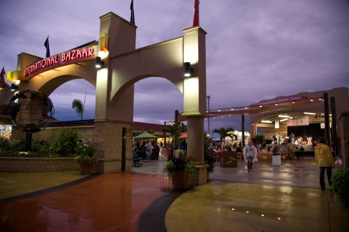 A lively outdoor market scene with an archway labeled "Emotional Bazaar," featuring vendors and a stage in the background.
