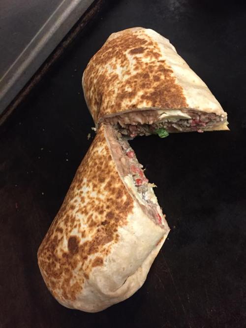 A toasted burrito cut in half, revealing a colorful filling of meat, beans, and vegetables.