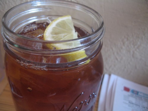 A close-up of a mason jar filled with iced tea and a slice of lemon on top.