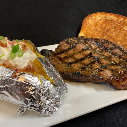 A grilled steak with a baked potato topped with cheese and green onions, alongside a slice of toasted bread.