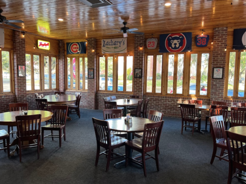 Interior of a restaurant with wooden tables, chairs, and brick walls, featuring sports memorabilia and large windows.