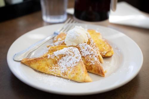 Plate of French toast triangles dusted with powdered sugar and topped with whipped cream, served with a fork.