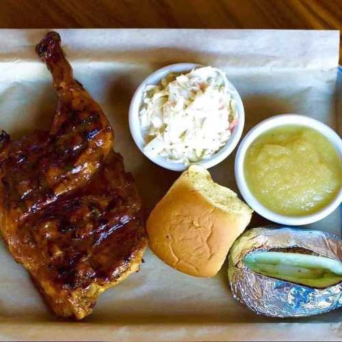 A tray with grilled chicken, coleslaw, applesauce, a roll, and a baked potato wrapped in foil.