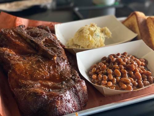 A plate featuring smoked meat, baked beans, mashed potatoes, and toasted bread, served on a tray.