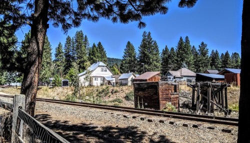 A view of a rural area with a house, trees, and a railway track under a clear blue sky.