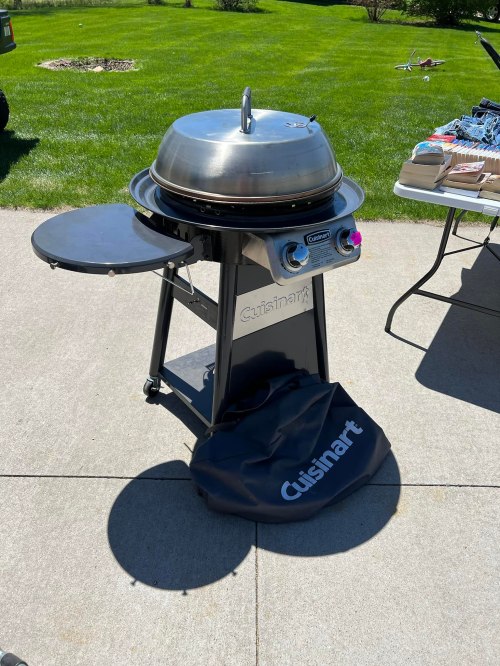 A Cuisinart grill on a patio, featuring a dome lid and side table, with a black cover on the ground.