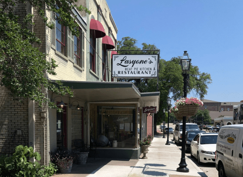 A quaint restaurant exterior with a sign reading "Lasyone's Meat Pie Kitchen & Restaurant" on a sunny street.