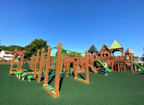 A colorful playground with slides and climbing structures on a sunny day, surrounded by green grass.