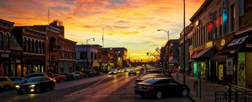 A vibrant sunset over a bustling street lined with shops and parked cars, creating a warm, inviting atmosphere.