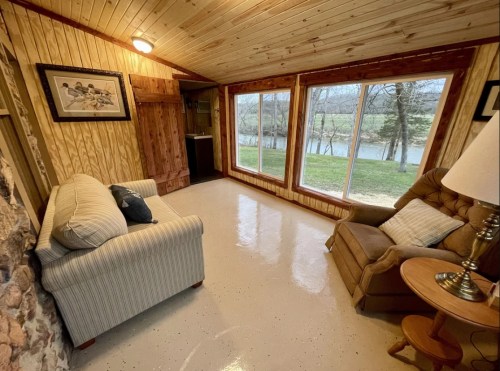 Cozy living space with a striped sofa, armchair, and large windows overlooking a serene outdoor view.