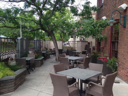 Outdoor dining area with tables and chairs surrounded by greenery and brick walls.