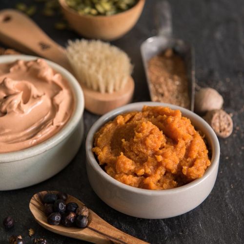 Two bowls of creamy spreads: one with a light brown paste and the other with a vibrant orange puree, surrounded by spices.