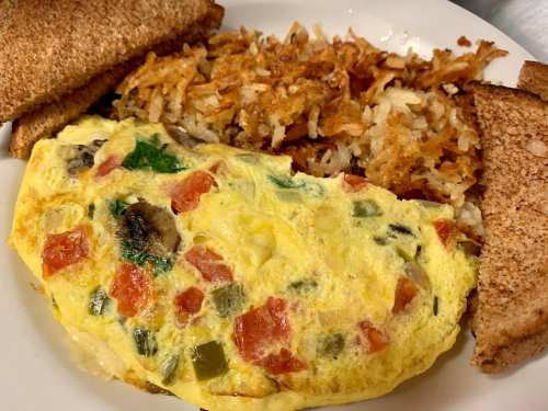 A plate with a vegetable omelette, crispy hash browns, and slices of toasted bread.