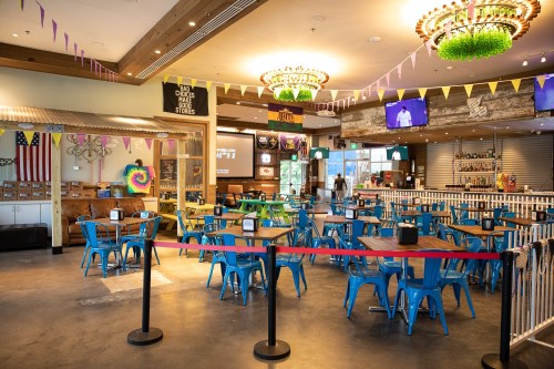 A spacious restaurant with blue chairs and tables, colorful decorations, and a bar area, set up for dining.