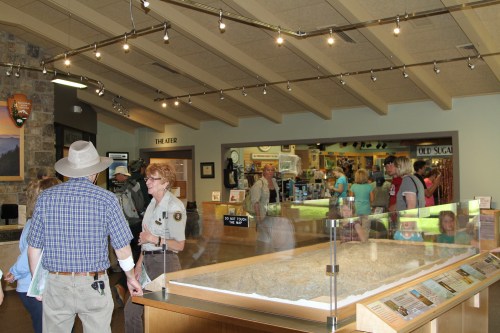 A busy visitor center with people interacting, a display case, and informational signs in a well-lit space.