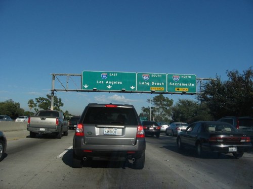 Traffic on a highway with signs for Los Angeles, Long Beach, and Sacramento under a clear blue sky.