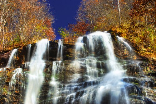 A cascading waterfall surrounded by vibrant autumn foliage under a clear blue sky.