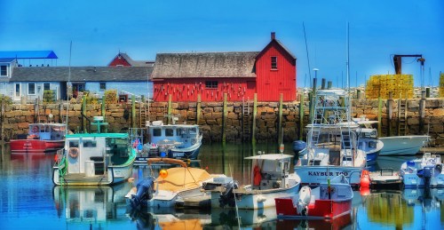 Colorful fishing boats docked in a serene harbor, with a red building and rocky shoreline in the background.
