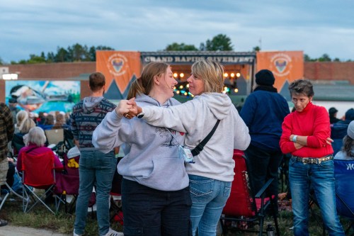 Two women dance together at an outdoor concert, surrounded by an audience enjoying the performance.