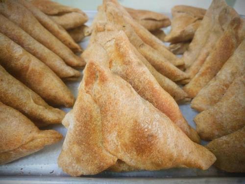 A close-up of golden-brown, triangular samosas arranged on a tray.