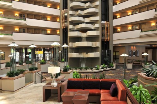 A spacious hotel lobby featuring a central water fountain, plants, and modern seating areas.
