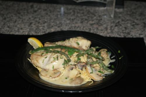 A plate of creamy chicken with mushrooms and asparagus, served over pasta, garnished with parsley and a lemon wedge.