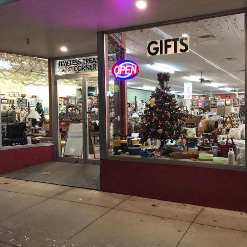 A storefront with a sign reading "Gifts" and a lit "Open" sign, featuring a decorated Christmas tree inside.