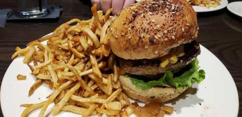 A sesame seed bun burger with lettuce, cheese, and caramelized onions, served with a side of crispy French fries.