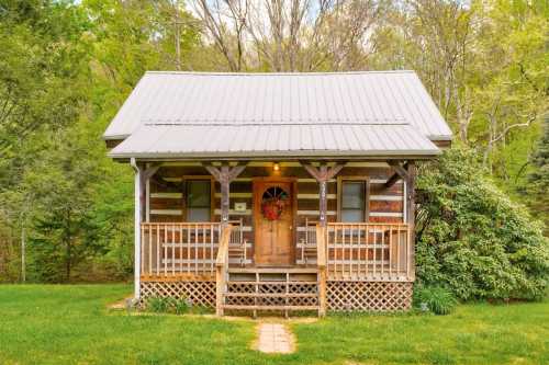 A charming log cabin with a metal roof, front porch, and a wreath on the door, surrounded by greenery.