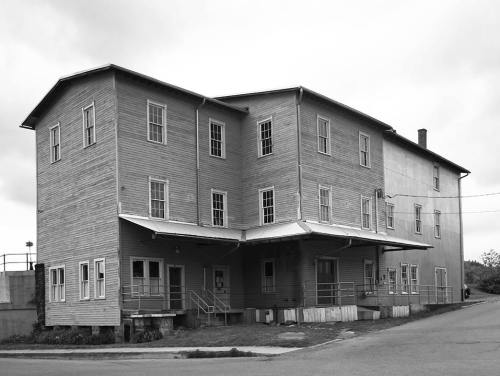 A large, two-story wooden building with multiple windows and a covered entrance, set against a cloudy sky.