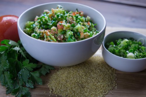 A bowl of tabbouleh salad with parsley, tomatoes, and bulgur, alongside a small bowl of chopped green onions and fresh ingredients.