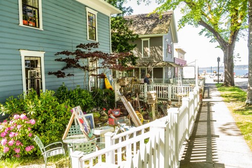 Charming street view of colorful houses, a garden, and a quaint shop with outdoor seating near a waterfront.