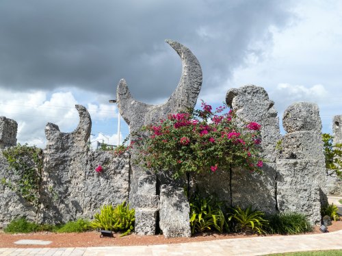 Stone sculptures with crescent shapes surrounded by vibrant flowers and greenery under a cloudy sky.