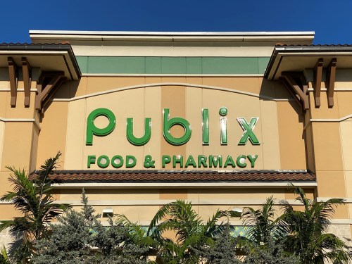 Signage of a Publix Food & Pharmacy store, featuring green letters against a tan building with palm trees in the foreground.