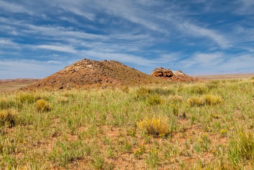 A grassy landscape features two small rocky hills under a blue sky with wispy clouds.