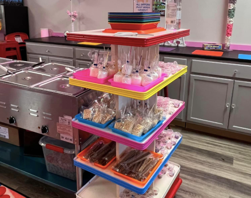 A colorful display stand filled with various treats, including candy, rice crispy treats, and lollipops.